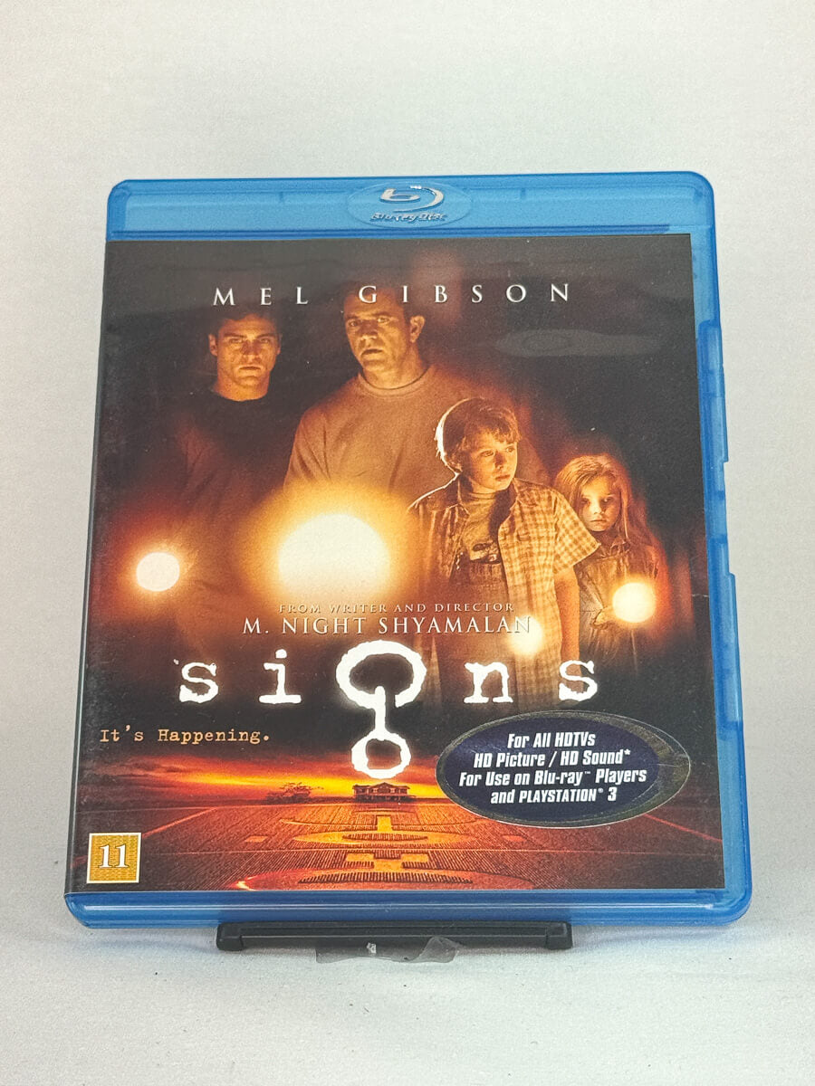 Forside av Blu-ray-cover til Signs – intens og stemningsfull sci-fi-thriller av M. Night Shyamalan med Mel Gibson i hovedrollen, brukt film hos Brukbar Film.