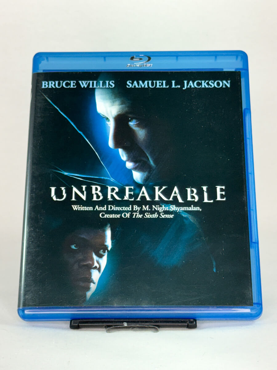 Forside av Blu-ray-cover til Unbreakable – original superhelt-thriller fra M. Night Shyamalan med Bruce Willis og Samuel L. Jackson, brukt film hos Brukbar Film.
