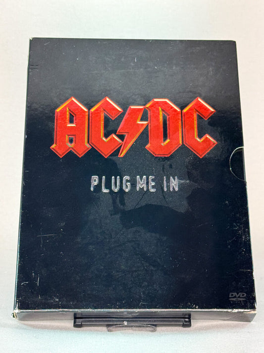 Forside av DVD-cover til AC/DC – Plug Me In – eksklusiv samleboks med liveopptredener og intervjuer fra bandets legendariske karriere, brukt musikkdokumentar på DVD hos Brukbar Film.