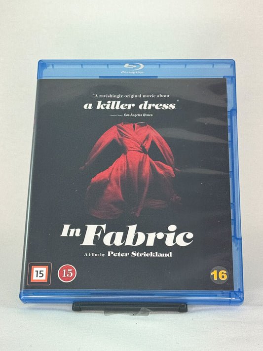Forside av Blu-ray-cover til In Fabric regissert av Peter Strickland – surrealistisk horrorfilm om en forbannet kjole, brukt Blu-ray hos Brukbar Film.