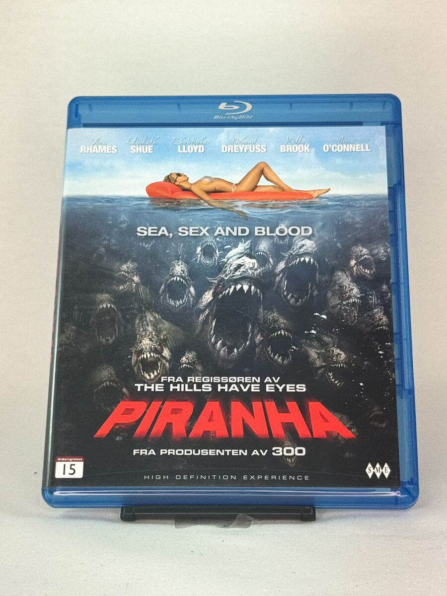 Forside av Blu-ray-cover til Piranha – blodig skrekkfilm fylt med humor og effekter fra produsenten av 300, brukt Blu-ray hos Brukbar Film.