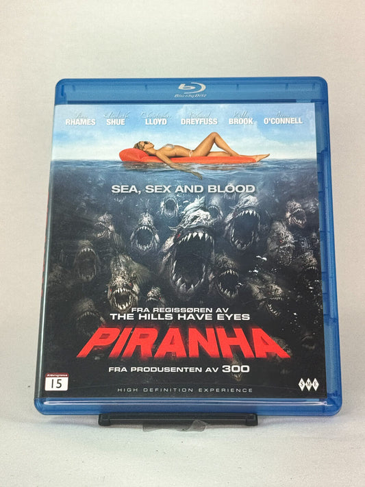Forside av Blu-ray-cover til Piranha – blodig skrekkfilm fylt med humor og effekter fra produsenten av 300, brukt Blu-ray hos Brukbar Film.