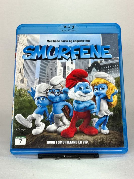 Forside av Blu-ray-cover til Smurfene – eventyrlig familiefilm der de blå figurene havner midt i New York, med både norsk og engelsk tale, brukt Blu-ray hos Brukbar Film.