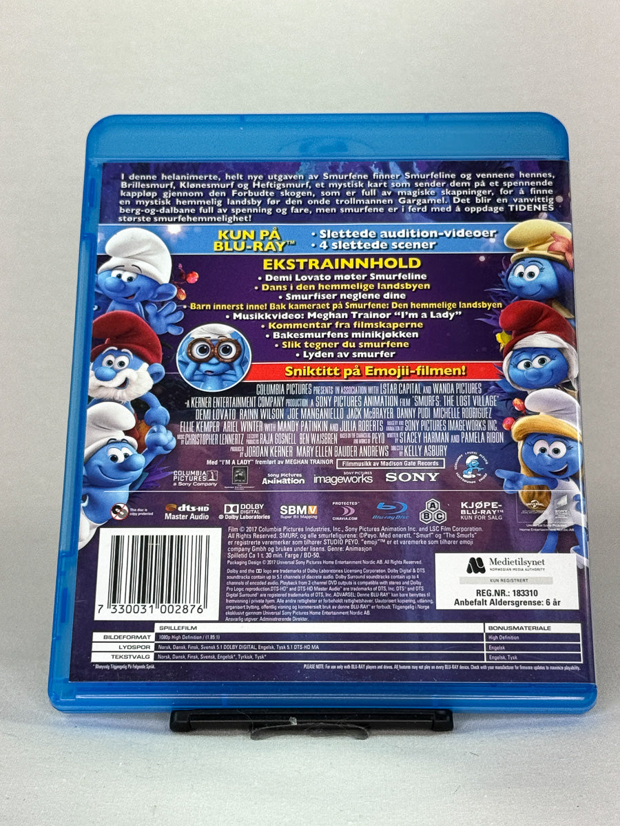 Bakside av Blu-ray-cover til Smurfene – Den hemmelige landsbyen – familievennlig animasjonsfilm fylt med eventyr, humor og magi, brukt Blu-ray-utgave tilgjengelig hos Brukbar Film.