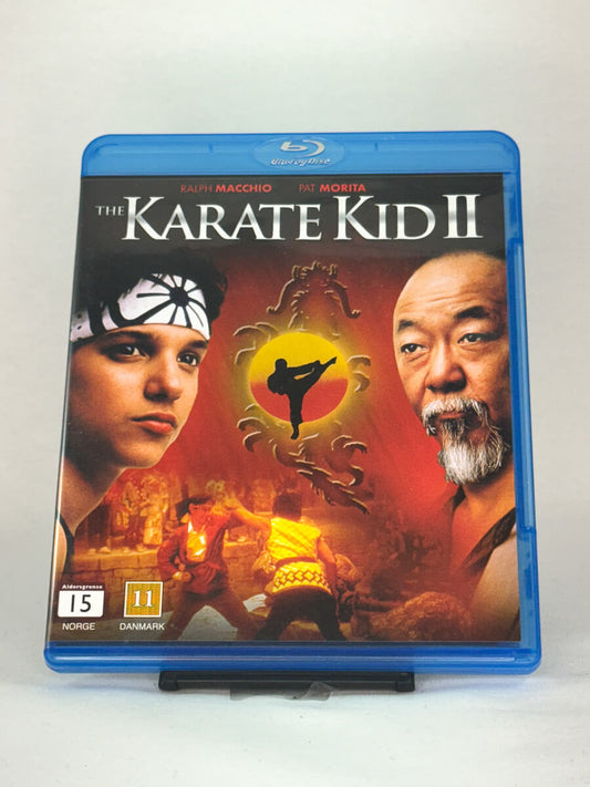Forside av Blu-ray-cover til The Karate Kid II – oppfølgeren der Daniel og Mr. Miyagi reiser til Okinawa for nye prøvelser, brukt Blu-ray hos Brukbar Film.