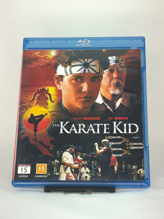 Forside av Blu-ray-cover til The Karate Kid – 80-tallsklassiker med Ralph Macchio og Pat Morita, kjent for sin inspirerende kamptrening og ikoniske øyeblikk, brukt Blu-ray hos Brukbar Film.