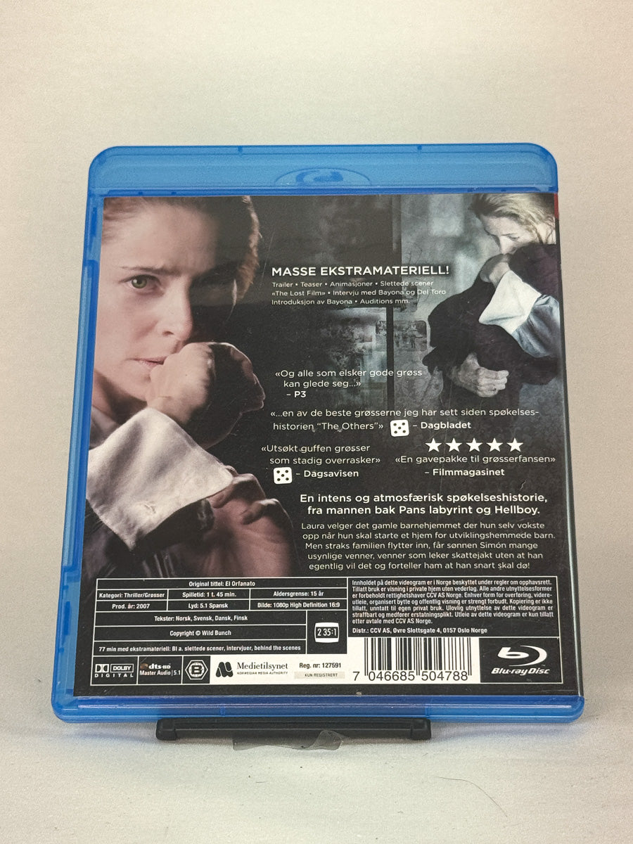 Bakside av Blu-ray-cover til The Orphanage – stemningsfull og skremmende thriller regissert av J.A. Bayona, brukt Blu-ray-film tilgjengelig hos Brukbar Film.
